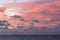 Sunrise with pink sky and clouds and a lighthouse in the horizon