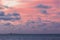 Sunrise with pink sky and clouds and a lighthouse in the horizon