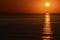 The sunrise from the sea, with the sun on right, orange sky and long reflection on the surface of water