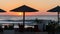 Sunrise on the seafront with reed sun silhouette umbrellas, the sea with waves and dinner table