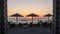 Sunrise on the seafront with reed sun silhouette umbrellas, the sea with waves and dinner table