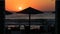 Sunrise on the seafront with reed sun silhouette umbrellas, the sea with waves and dinner table