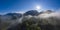 Sunrise sunbeams over foggy mountains with clouds between forest trees