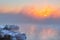 Sunrise time over the winter river. An orange fog spreads over the water and obscures the horizon. Reeds stand in the snow near