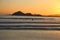 Sunset at the beach. In the background silhouettes of mountains, reddish sky. Beach with reflections in the sand.