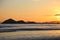 Sunset at the beach. In the background silhouettes of mountains, reddish sky. Beach with reflections in the sand.