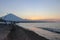 Sunset on the beach on a tropical island. Orange colored sky and clouds. Big majestic volcano on the horizon.