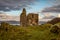 Sunset behind Castle Tarbert in the middle of the picture with rough lumpy rolling grass and rocks in the foreground