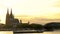 Sunset behind Cologne Cathedral and a train on Hohenzollern Bridge with boats sailing on the River Rhine, Germany