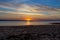 Sunset behind a distant cape, view from a deserted sandy shore