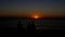 Sunset. The bright sun sets over the horizon in the sea. Silhouettes of people sitting on the beach against the sea at sunset.