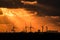 Sunset casting rays through a dramatic orange cloudy sky, onto backlit electric windmills