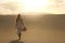 Sunset in the desert. Young woman with white dress walking in the desert dunes with footsteps in the sand during sunset. Girl