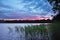 Sunset on the lake in evening twilght. Reeds on the coast. Summer rural landscape.