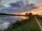 SUNSET,LAKE,GRAY CLOUDS, REFLECTION  OF ALL THESE ON LAKE& x27;S WATER,A GREEN GRASSY ROAD