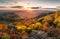 Sunset landscape with high peaks and valley with autumn spruce forest under vibrant colorful evening sky in forest mountains