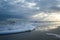 Sunset with Light Beams over the Ocean with Foamy Waves on the Beach