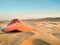 sunset light of a red cap abandoned or forgotten on the brown sand of dune of the desert by a tourist person on holidays. The wind