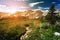 Sunset light shining behind a distant mountain range and a dirt hiking trail winding through an alpine meadow in Colorado