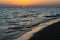 Sunset on the Mediterranean Sea in Greece with calm ocean water and dark sand beach in the foreground