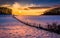 Sunset over a fence in a snow covered farm field in rural Carroll County, Maryland.