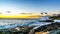 Sunset over the horizon with a few clouds and the rocky shores of the west coast of Oahu