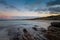 Sunset over the picturesque white sand beach and turquoise waters at La Pelosa Beach with rocks in the foreground