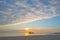 Sunset over sea along a beach below a blue cloudy sky at fall