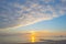 Sunset over sea along a beach below a blue cloudy sky at fall