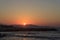 Sunset over the sea in Kokkini Hani, Crete, Greece. The sun disappears behind the mountain. Scenic seaside landscape in the