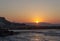 Sunset over the sea in Kokkini Hani, Crete, Greece. The sun disappears behind the mountain. Scenic seaside landscape in the