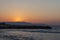 Sunset over the sea in Kokkini Hani, Crete, Greece. The sun disappears behind the mountain. Scenic seaside landscape in the