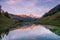 Sunset over Snowy Mountains and Wood Chalet Reflecting in Altitude Lake.