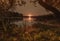Sunset over water with reflection and sunbeams in nature in summer with trees and grass. Calm peaceful landscape with