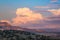 Sunset paints cumulus clouds and thunderheads in soft colors of pink, purple and peach over a colorful desert landscape