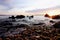 Sunset at pebble beach and big rock emerging from the sea with dramatic clouds on the sky