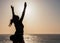 Sunset Reverie: Woman\\\'s Pose on the Beach, Arms Raised, with Descending Sun and Distant Fishermen