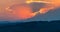 Sunset scene with sun fall behind the clouds and mountains in background, warm colorful sky with