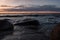 At sunset, sea waves break on the coastal granite stones.