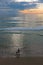 Sunset seascape, orange, blue, yellow sky, with aqua marine green sea, white waves rolling in, surfer at dusk walking in the surf