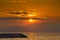 Sunset on the seashore. The fiery setting sun illuminates the mountains, the sea and the rocky pier