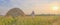 At sunset an senior Muslim man in an embroidered skullcap and white traditional Clothes mows hand-scythe grass in a hayfield