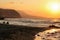 Sunset shines to two sunbeds on empty wild beach. Small sea waves, hills in hazy background