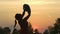 Sunset Silhouette: Young mother holding her baby boy child in city park standing in front of setting sun and vivid