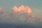 Sunset sky with billowing pink cloud with light shining through against turquoise sky above storm clouds