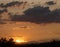 Sunset sky, dark clouds and the sun that descends over the horizon with bushes