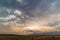 Sunset sky with dramatic clouds and a distant storm over a field