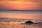 Sunset, small rock at low tide in front of the illuminated sea. Light waves