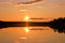 Sunset with strong colors. Lake, horizon, orange sky with cloudlets, glowing sun and reflection.