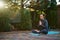 Sunset sunlight fall on backyard, while a man, yogi meditating in lotus position, on a yoga mat, keeping palms together